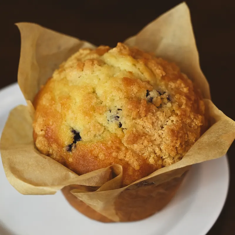A blueberry crumb muffin in a paper tulip liner on a white plate.
