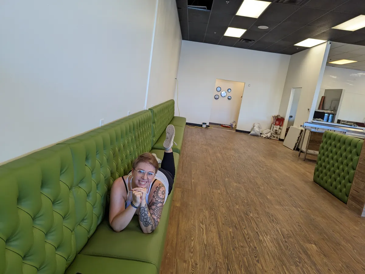 Somebody lying full length along the new green tufted banquette in the otherwise empty shop, grinning at the camera.