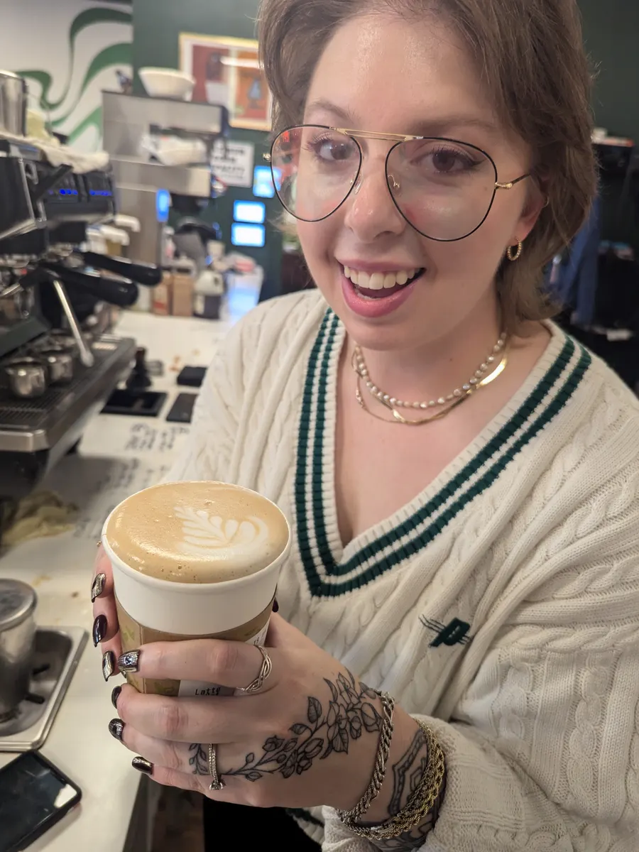 A barista holding up a latte with a leaf poured into the foam, smiling.