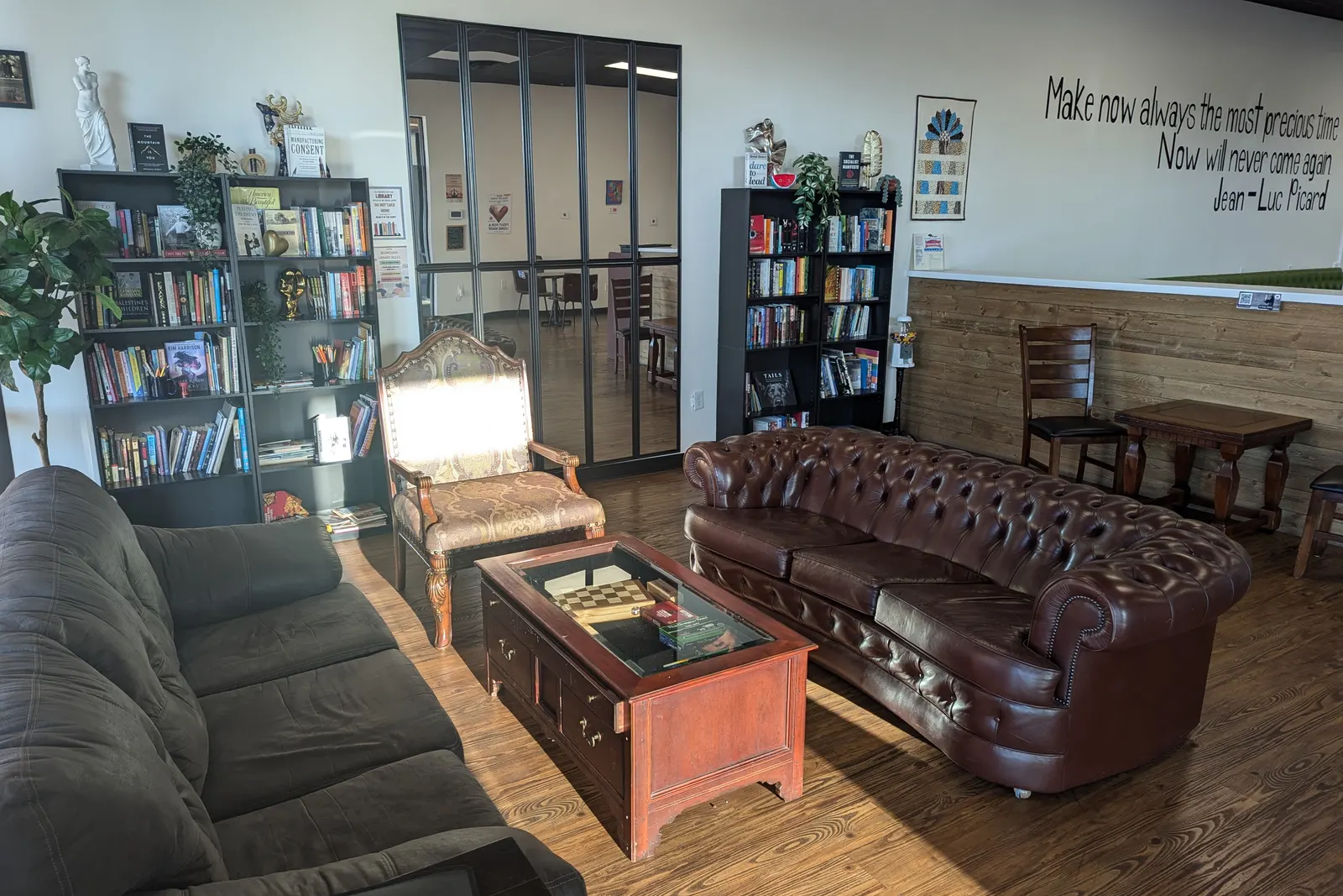 The lounge: a leather chesterfield and armchairs in front of full bookshelves, under a painted quote.
