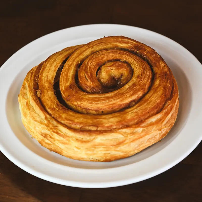 A cinnamon roll croissant on a white plate.