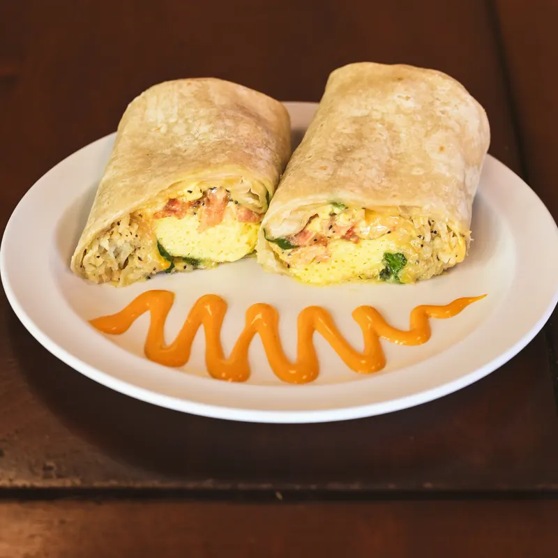 A breakfast burrito cut in half, served with a swirl of sriracha mayo.