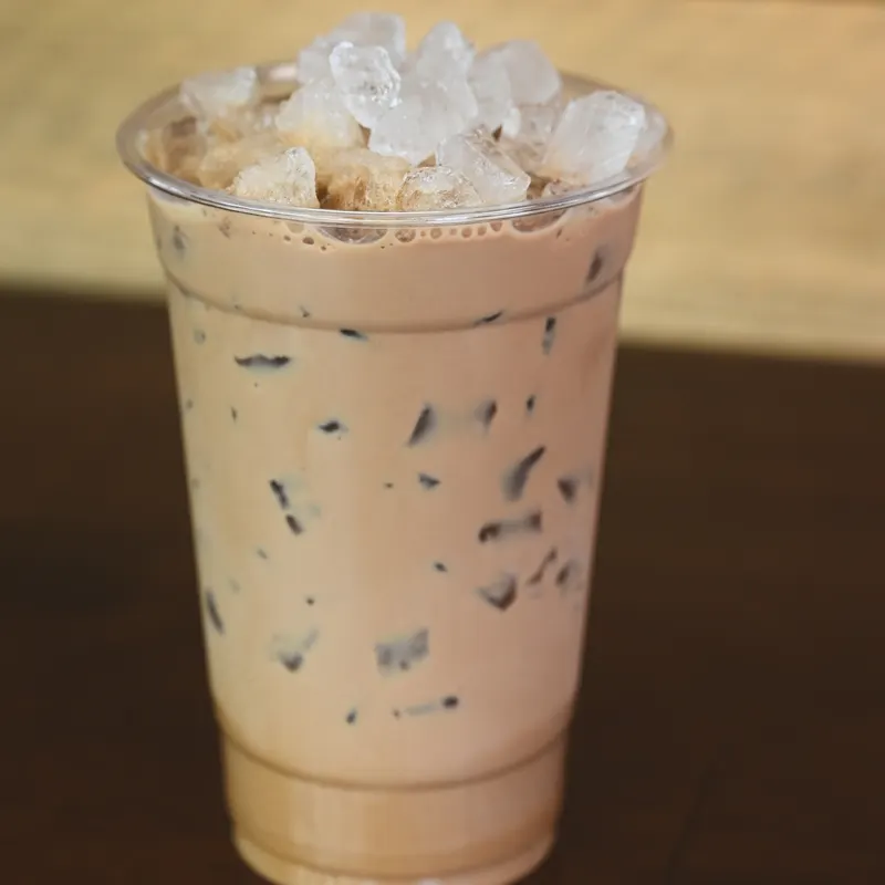 An iced coconut mocha in a clear cup on the wooden counter.