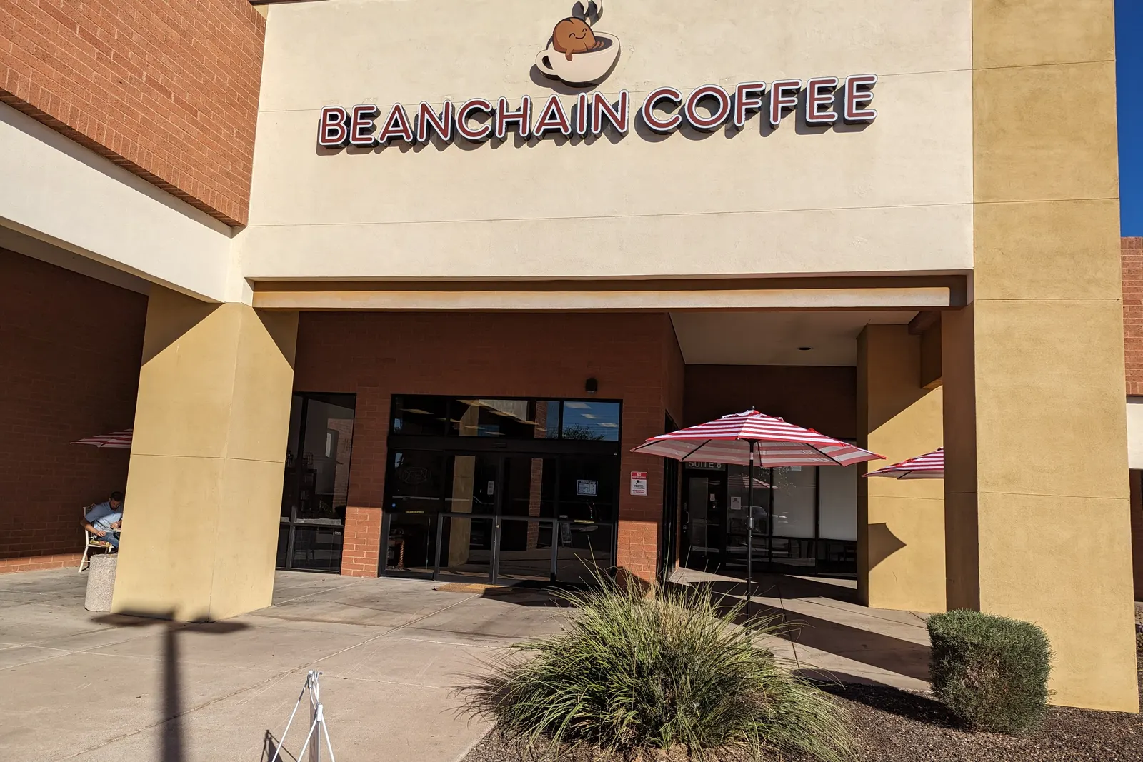 The Beanchain Coffee storefront, with the sign above the door and a red umbrella on the patio.